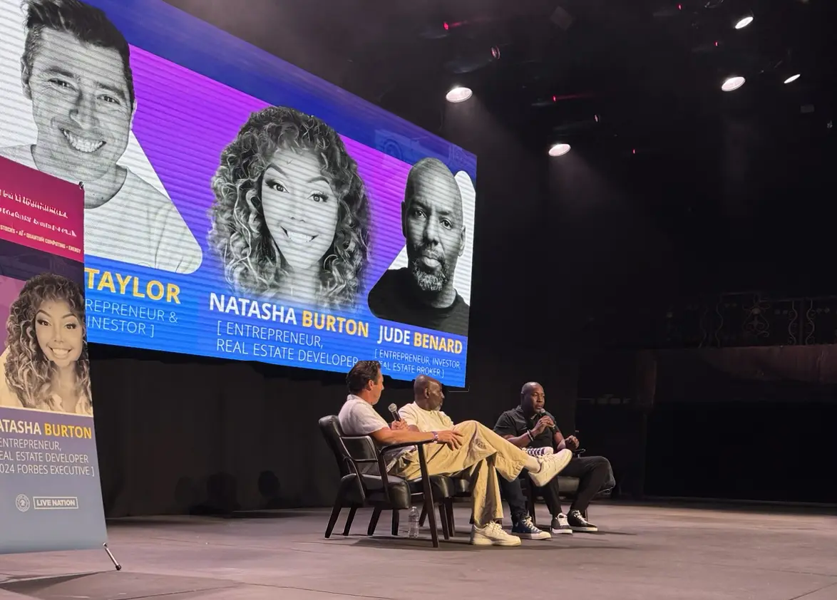 A panel of three speakers on stage at a previous event, under a screen naming a real estate developer and a real estate broker
